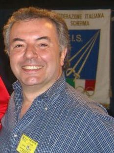 la foto mostra un uomo di mezza età con i capelli grigi, sorridente e con una camicia a quadretti.